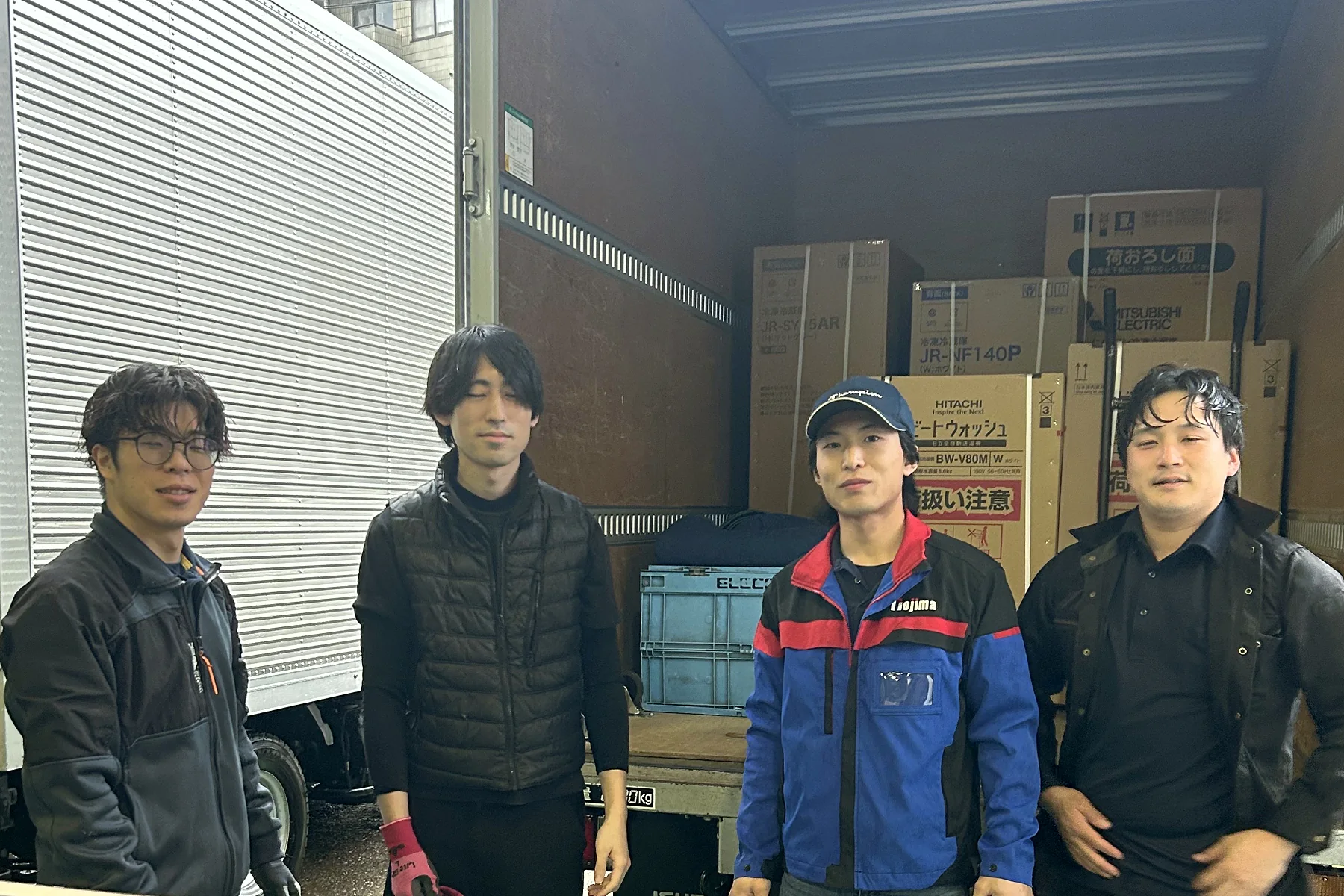浦安本社の車庫で、積み終えたトラックの前に並び、これから現場へ出る配送スタッフ四人
