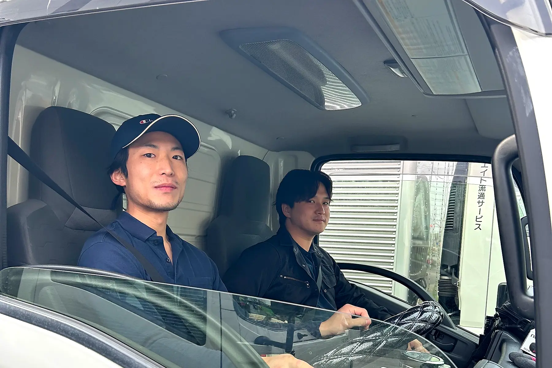 2tトラックの運転席でハンドルを握る社員と助手席の社員